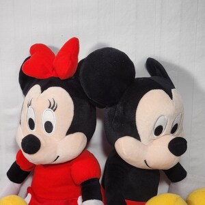 Pu&ograve; includere: Due bambole di peluche dei personaggi Disney: Minnie Mouse e Topolino. Minnie indossa un vestito rosso a pois bianchi e un fiocco rosso. Topolino indossa pantaloncini neri, giacca nera e guanti bianchi. Entrambi hanno orecchie nere e facce sorridenti.