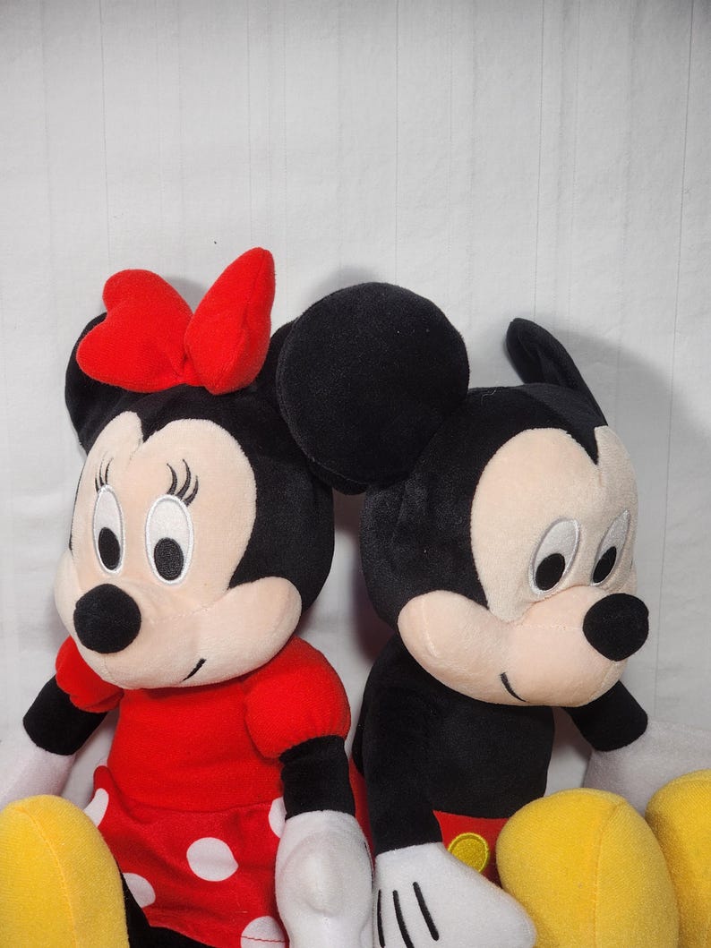 Pu&ograve; includere: Due bambole di peluche dei personaggi Disney: Minnie Mouse e Topolino. Minnie indossa un vestito rosso a pois bianchi e un fiocco rosso. Topolino indossa pantaloncini neri, giacca nera e guanti bianchi. Entrambi hanno orecchie nere e facce sorridenti.
