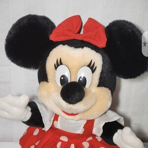 May include: A plush Minnie Mouse doll with black ears, a red bow, and a red dress with white polka dots. The doll has white gloves and a smiling expression. A classic Disney character.