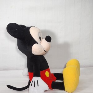 Pu&ograve; includere: Un peluche di Topolino in posizione seduta. Il giocattolo presenta un corpo, orecchie e coda neri, con un viso e mani bianche. Mickey indossa pantaloncini rossi, un bottone giallo e scarpe gialle. Il giocattolo &egrave; morbido e coccoloso.