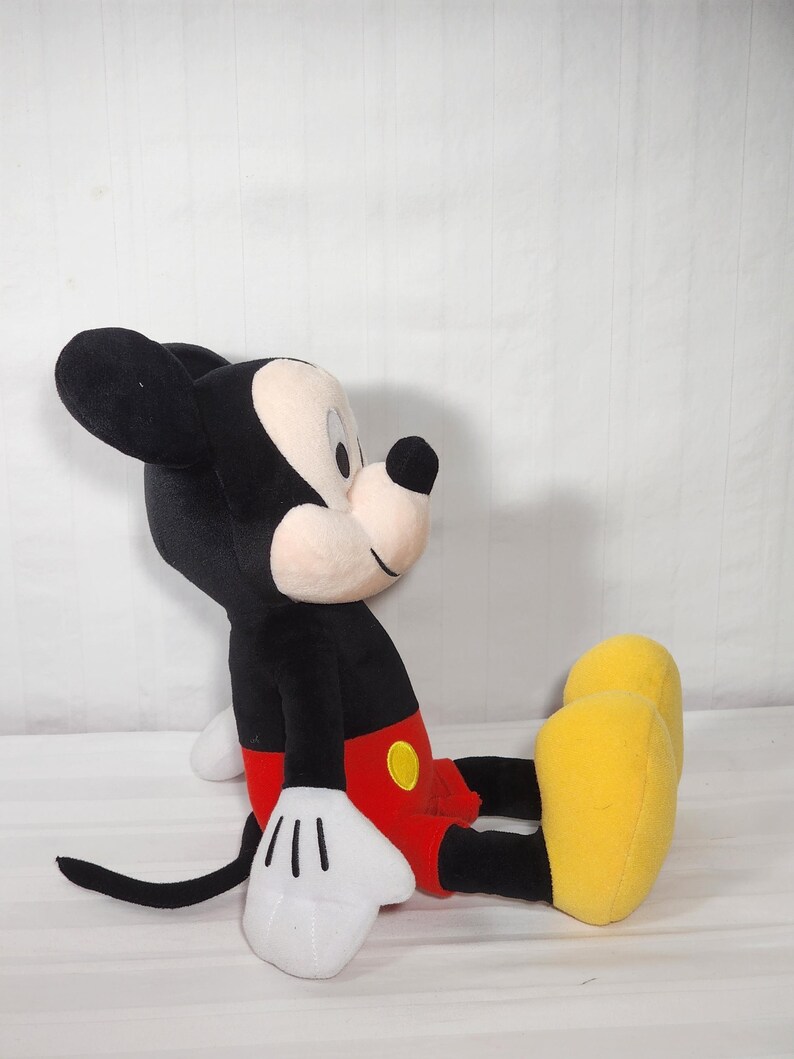 Pu&ograve; includere: Un peluche di Topolino in posizione seduta. Il giocattolo presenta un corpo, orecchie e coda neri, con un viso e mani bianche. Mickey indossa pantaloncini rossi, un bottone giallo e scarpe gialle. Il giocattolo &egrave; morbido e coccoloso.