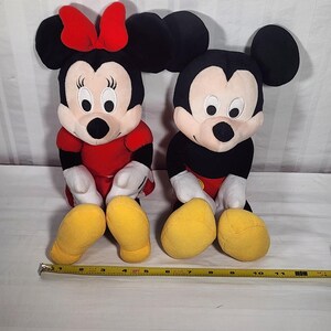 Pu&ograve; includere: Due bambole di peluche dei personaggi Disney, Minnie Mouse e Topolino, sono sedute fianco a fianco. Minnie indossa un vestito e un fiocco rossi, mentre Topolino ha pantaloncini rossi. Entrambi hanno orecchie nere, guanti bianchi e scarpe gialle.