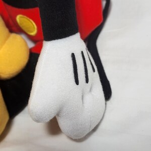 Pu&ograve; includere: Primo piano di una mano di peluche bianca con linee nere che rappresentano le dita. La mano fa parte di un giocattolo pi&ugrave; grande con elementi rossi, neri e gialli, probabilmente un personaggio dei cartoni animati.
