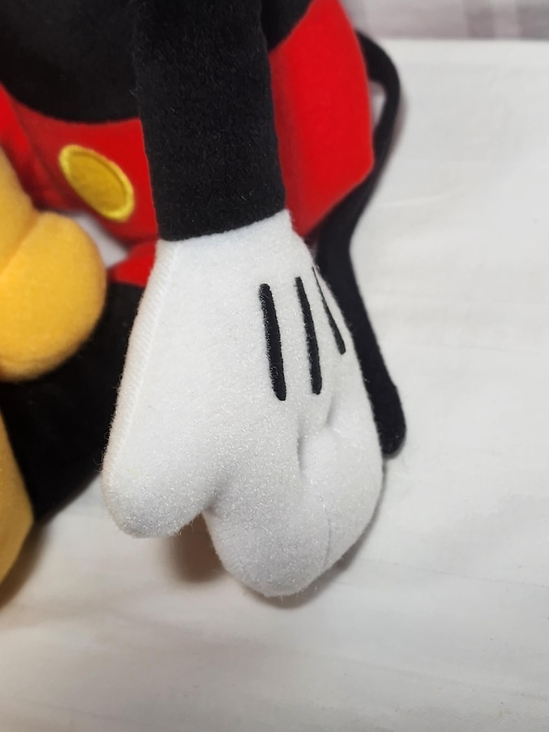 Pu&ograve; includere: Primo piano di una mano di peluche bianca con linee nere che rappresentano le dita. La mano fa parte di un giocattolo pi&ugrave; grande con elementi rossi, neri e gialli, probabilmente un personaggio dei cartoni animati.