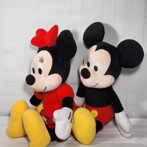 Pu&ograve; includere: Due peluche Disney, Topolino e Minnie, sono seduti uno accanto all'altro. Topolino &egrave; in nero, rosso e giallo, mentre Minnie indossa un fiocco e un vestito rossi. Entrambi hanno grandi orecchie nere, guanti bianchi e scarpe gialle.