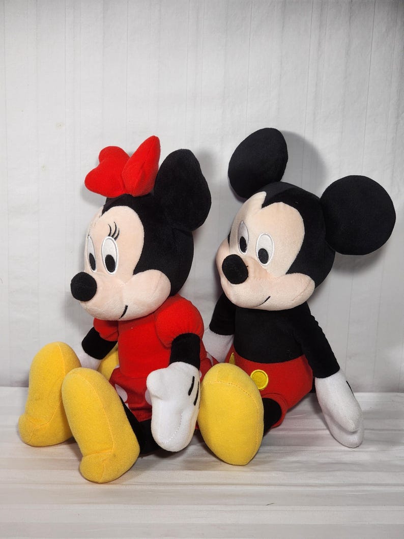Pu&ograve; includere: Due peluche Disney, Topolino e Minnie, sono seduti uno accanto all'altro. Topolino &egrave; in nero, rosso e giallo, mentre Minnie indossa un fiocco e un vestito rossi. Entrambi hanno grandi orecchie nere, guanti bianchi e scarpe gialle.