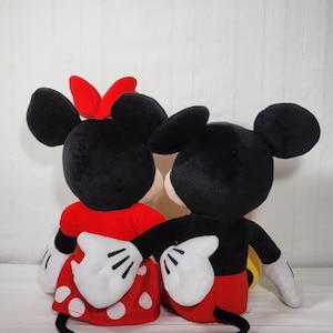 Pu&ograve; includere: Due peluche di Topolino e Minnie Mouse. Topolino indossa pantaloncini rossi, una giacca nera e guanti bianchi. Minnie indossa un vestito rosso a pois bianchi, un fiocco rosso e guanti bianchi. Entrambi hanno orecchie nere.