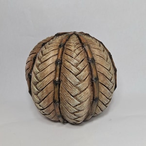 May include: A spherical decorative object featuring a woven tan texture in a herringbone pattern, segmented by vertical dark brown bamboo-like ribs that converge at the top and bottom poles, creating a structured, multi-paneled appearance.