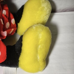 May include: Close-up of a plush toy's yellow feet and black legs. The feet are a bright yellow color, and the legs are black. A red polka-dot dress is visible on the left side of the image. The toy is likely a character from a popular cartoon.