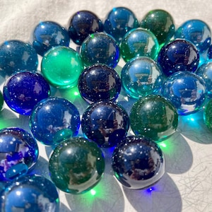 May include: A collection of blue and green glass marbles. The marbles are iridescent and have a variety of shades of blue and green.