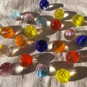 Op de afbeelding: Een verzameling kleurrijke glazen knikkers met bloemmotieven. De knikkers zijn gerangschikt op een wit stoffen oppervlak.