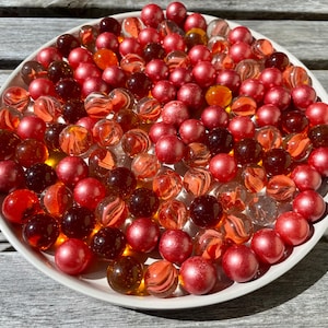 May include: A white bowl filled with red, orange, and clear glass marbles. The marbles are arranged in a random pattern.