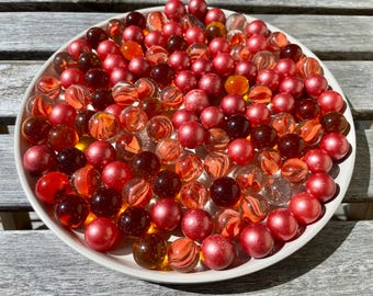 May include: A white bowl filled with red, orange, and clear glass marbles. The marbles are arranged in a random pattern.