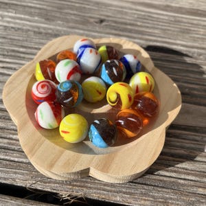 Op de afbeelding: Een verzameling kleurrijke glazen knikkers in een houten kom. De knikkers zijn in verschillende tinten rood, blauw, geel en oranje met witte swirls.