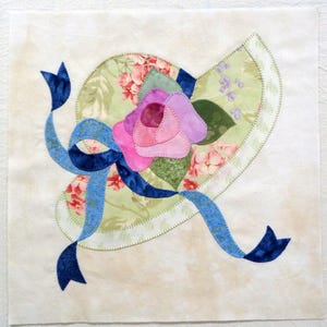 May include: A green and white floral fabric hat with a blue ribbon and a pink and purple flower.