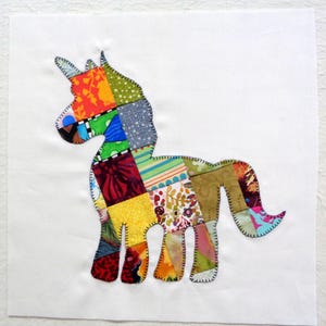 May include: A colorful patchwork unicorn applique on a white background. The unicorn is composed of various fabric scraps in shades of red, orange, yellow, green, blue, and brown. The edges are stitched with black thread.
