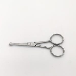 May include: Silver-toned grooming scissors with rounded tips and a small hole near the pivot point. The scissors have the word "SOLINGEN" engraved on the side.