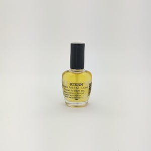 Könnte beinhalten: Kleine, transparente Flasche Stern Pastix Art. 142, mit 12,5 ml gelber Flüssigkeit. Die Flasche hat einen schwarzen Deckel und ein Etikett mit deutschem Text. Das Produkt dient zum Kleben von Bärten und ist brennbar.