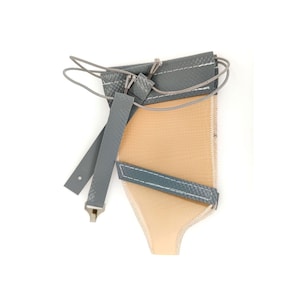 May include: A gray and beige pouch with a drawstring closure and two gray straps. The pouch is made of a durable material and has white stitching along the edges. The straps have a metal clasp.