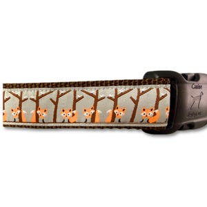 May include: Dog collar featuring a repeating pattern of orange foxes and brown trees on a light beige background. The collar has a brown border and a black buckle with the text "Canine Designs".