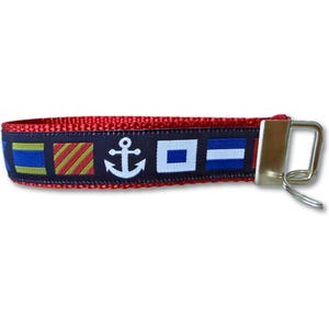 May include: Red nautical-themed wristlet key fob with a navy blue band featuring white anchor and flag designs. The key fob has a silver-colored metal clasp and a small key ring.