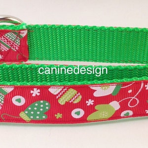 May include: A red and green dog collar with a festive Christmas pattern of mittens and snowflakes. The collar has a black buckle and a green webbing.