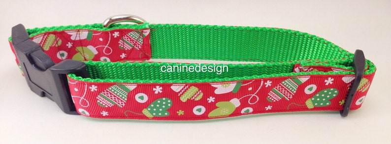 May include: A red and green dog collar with a festive Christmas pattern of mittens and snowflakes. The collar has a black buckle and a green webbing.
