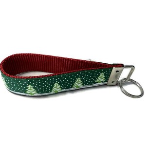 May include: A red and green Christmas-themed wristlet keychain. The wrist strap is red on the inside and green on the outside, with a pattern of white polka dots and green Christmas trees. A silver metal key ring is attached.