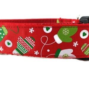 May include: Red dog collar with a Christmas pattern featuring green mittens, snowflakes, and white hearts.