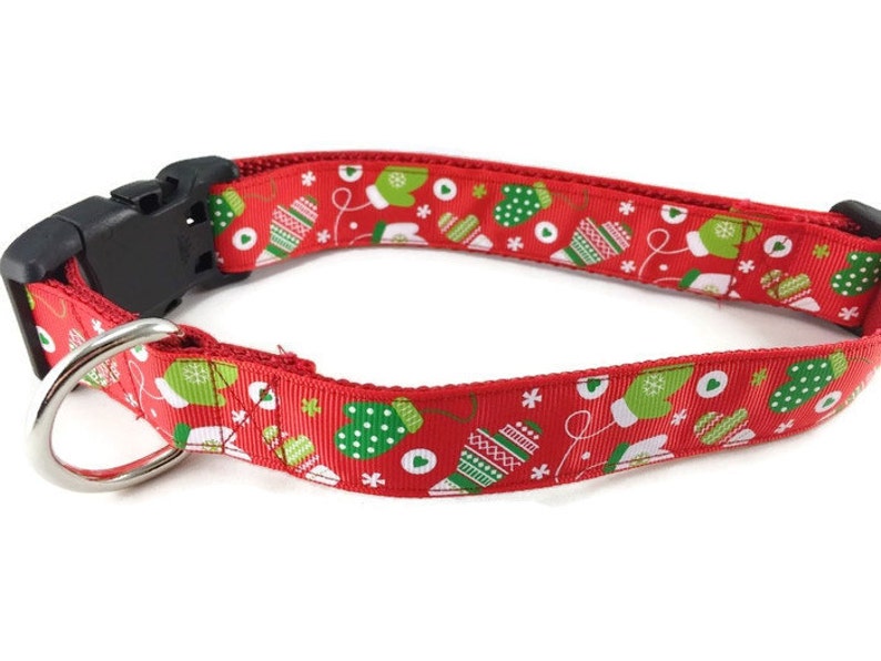 May include: Red dog collar with a Christmas mitten pattern. The collar has a black plastic buckle and a silver D-ring.