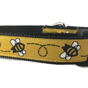 May include: A black dog collar with a yellow and black bee design. The collar has a black plastic buckle.