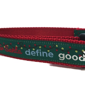 May include: Red and green dog collar with a Christmas theme. The collar has a green ribbon with white text that says "Dear Santa define good" and a string of white lights. There are small red Santa hats on either end of the ribbon.