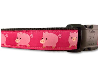 May include: A dog collar with a repeating pattern of pink cartoon pigs on a bright pink background. The collar has a black nylon backing and a black plastic buckle. The buckle is marked with the text "Canine designs.us".