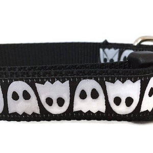 May include: Black dog collar with a white ghost pattern. The collar has a black plastic buckle.