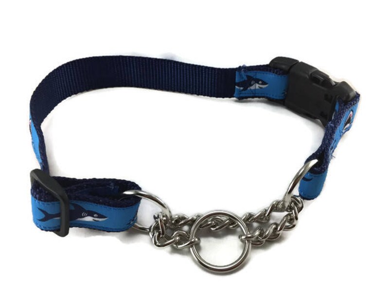 May include: Navy blue dog collar with a shark pattern on light blue accents. The collar features a black plastic buckle and a silver metal chain for leash attachment. A stylish accessory for your pet.