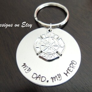May include: Silver keychain with a firefighter's emblem and the inscription "My Dad. My Hero."