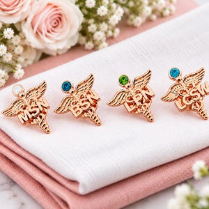 Puede incluir: Cuatro broches m&eacute;dicos de metal en tono oro rosa con forma de caduceo, alas y serpientes. Cada broche muestra un acr&oacute;nimo diferente: MSN con una piedra blanca, BSN con una piedra azul, LPN con una piedra verde y LCSW con una piedra azul.