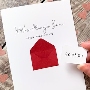 May include: A white anniversary greeting card featuring the black text It Was Always You and Happy Anniversary. A small red envelope is attached to the centre, and a separate white card insert displays the black printed date 20.05.20.