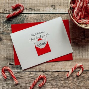 May include: A Christmas card with a red envelope and a white card that reads "This Christmas, I have loved you for..." with "11,675 DAYS" in a red envelope. Several red and white candy canes are scattered around the card.