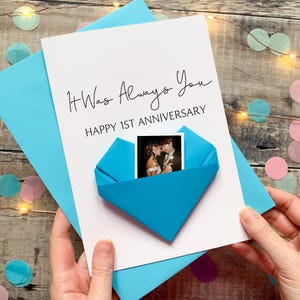 A handmade card with a photo of a couple inside a blue envelope, celebrating a first anniversary.