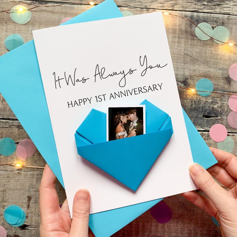 A handmade card with a photo of a couple inside a blue envelope, celebrating a first anniversary.