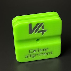 Può includere: Strumento di allineamento pinza verde brillante con il testo "V4" e "Caliper alignment" stampato sul davanti. Lo strumento è rettangolare con bordi arrotondati e una parte superiore scanalata. Il testo è grigio scuro.