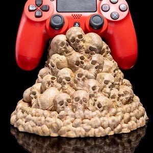 Könnte beinhalten: Ein roter PlayStation 4-Controller sitzt auf einem Schädel-förmigen Ständer. Der Ständer ist aus hellbraunem Material gefertigt und mit Dutzenden kleiner Schädel bedeckt.