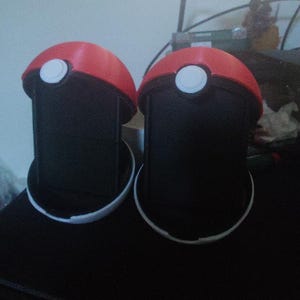 May include: Two red and white novelty containers, resembling a popular cartoon ball, are displayed. Each container has a black cylindrical body and a white base. The containers are on a dark surface.