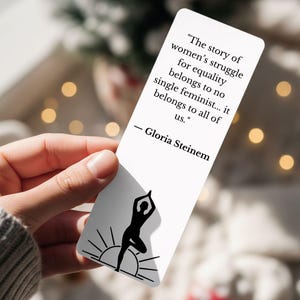 May include: A white bookmark with a quote by Gloria Steinem about women's equality. The bookmark features a black silhouette of a person in a yoga pose with a sun design. The text reads: "The story of women's struggle for equality belongs to no single feminist... it belongs to all of us."