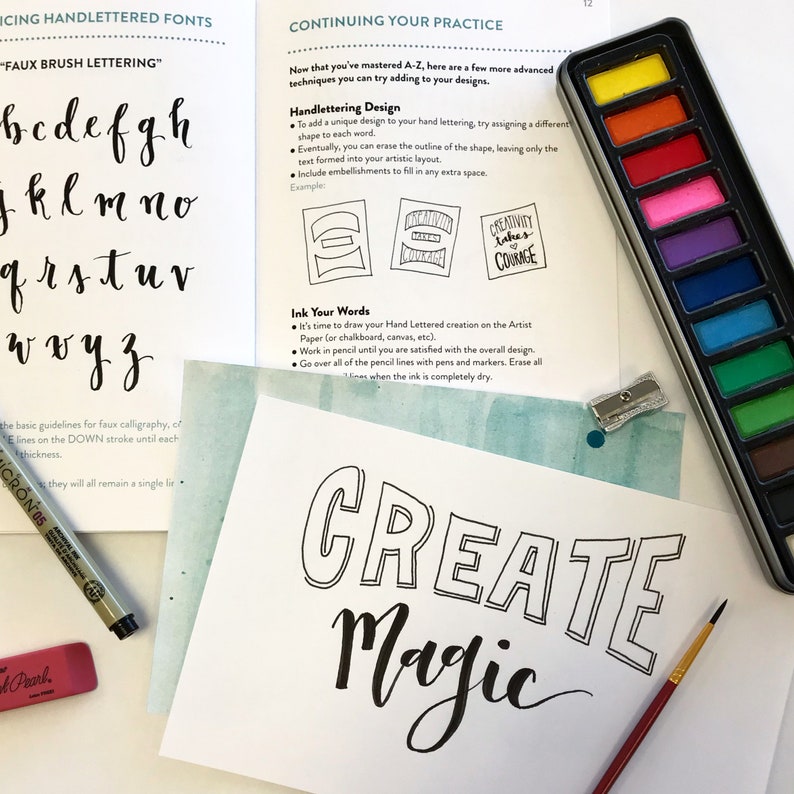 May include: A close-up of a sheet of paper with the words "CREATE MAGIC" written in black ink. The words are outlined in black and have a faux brush lettering style. A watercolor palette with 12 colors is visible in the background.