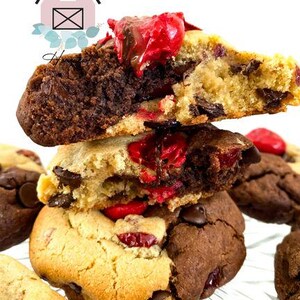 May include: Close-up of stacked cookies with chocolate chips and red cherries. The cookies are a mix of light and dark brown, with a soft, textured appearance. The top cookie is cut in half, revealing the interior.