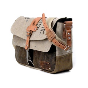 May include: A brown leather and canvas messenger bag with a long adjustable strap. The bag has a flap closure with a metal buckle and a small pocket on the front. The bag has a distressed look and is made of recycled materials.