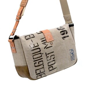 May include: A beige canvas messenger bag with a brown leather flap and strap. The bag has black printed text that reads "Post" and "1961".
