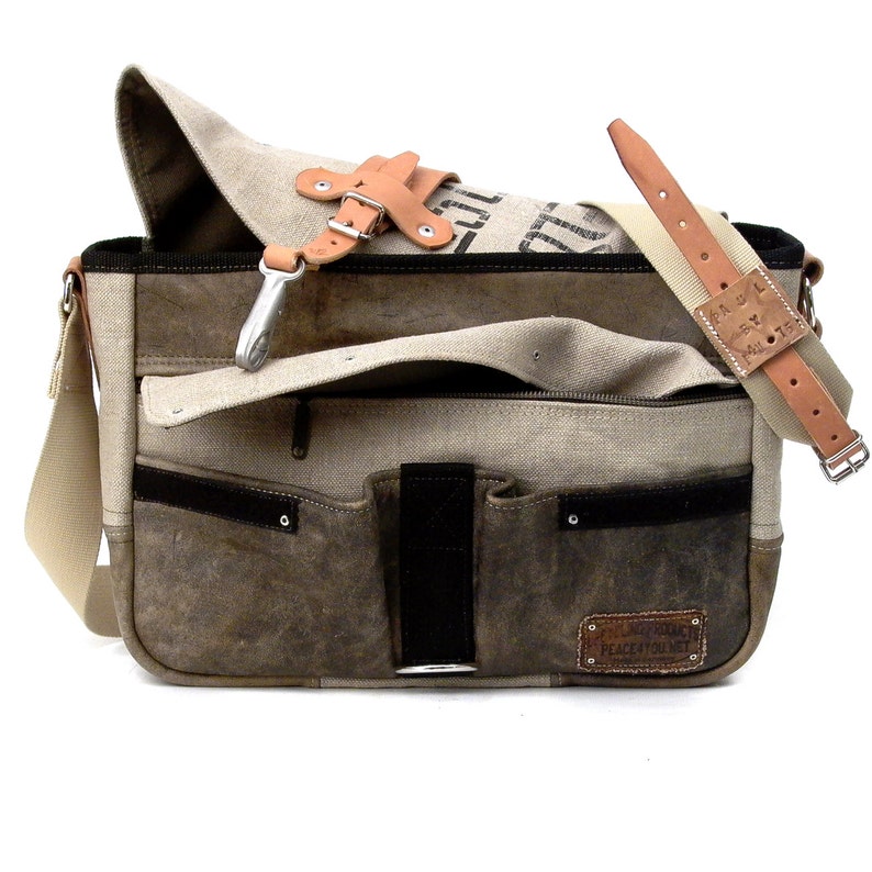 May include: A brown leather and canvas messenger bag with a large flap and multiple pockets. The bag has a brown leather strap and a metal buckle. The bag has a label that says "Remarkable Peace Movement".